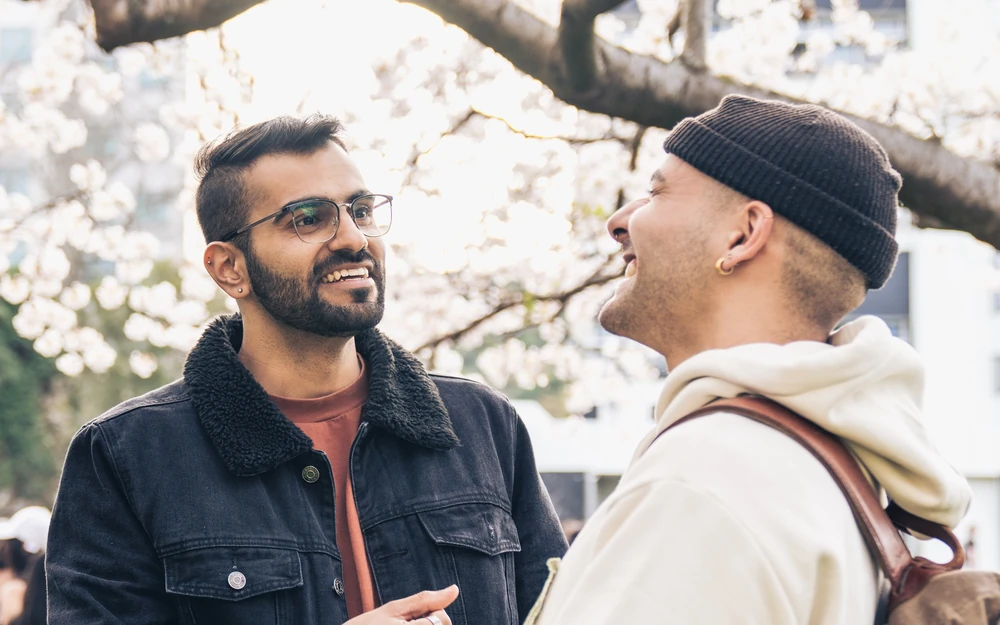 Two students stand under flowering trees and engage in a friendly conversation.